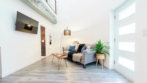 A modern living room with a sofa, a coffee table, a floor lamp, and a potted plant. - Restored Grain Bin with Hot Tub, King Bed, Vending Machine. Dog-friendly! (Rockbridge)