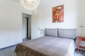 Une chambre à coucher avec un lit, une porte, une affiche accrochée au mur et une petite table.