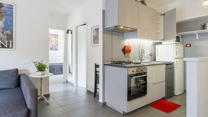 A compact kitchen with a stove, oven, and microwave, a small dining table, and a grey sofa.