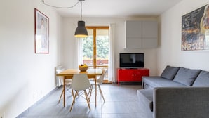 A modern living room with a sofa, a TV, a dining table with chairs, and a red cabinet.