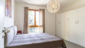 A bedroom with a bed, a wardrobe, a window with curtains, and a hanging light fixture.