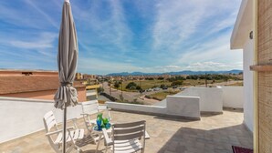 A terrace with a table, chairs, and an umbrella, overlooking a cityscape with mountains in the distance. - GuestHost - Cozy apartment of 65 sqm, able to accommodate up to 3 people, located on the second floor of a building without elevator. The property is equipped with every comfort, including air conditioning and a large terrace overlooking the city of Olbi (Olbia)