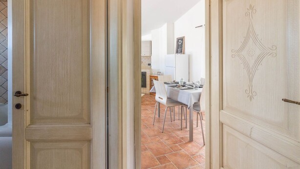 A room with a wooden door, a dining area with a table and chairs, and a kitchen in the background. - GuestHost - Cozy apartment of 65 sqm, able to accommodate up to 3 people, located on the second floor of a building without elevator. The property is equipped with every comfort, including air conditioning and a large terrace overlooking the city of Olbi (Olbia)