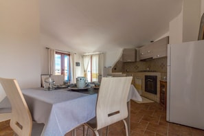 A dining area with a table set for two, a kitchen with a stove and refrigerator, and a window with curtains.