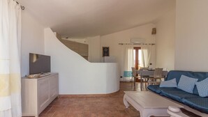 A living room with a sofa, a coffee table, a TV on a cabinet, a staircase, and a dining area with chairs and a table. - GuestHost - Cozy apartment of 65 sqm, able to accommodate up to 3 people, located on the second floor of a building without elevator. The property is equipped with every comfort, including air conditioning and a large terrace overlooking the city of Olbi (Olbia)