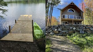 A wooden dock leading to a green kayak and a stone wall with a cabin featuring a balcony and a large arched window.