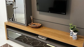 A modern entertainment unit with a flat-screen TV, a mirrored cabinet, and a built-in sound system. - Ap Gold Coast Vista Mar - Piçarras - SC (Picarras)
