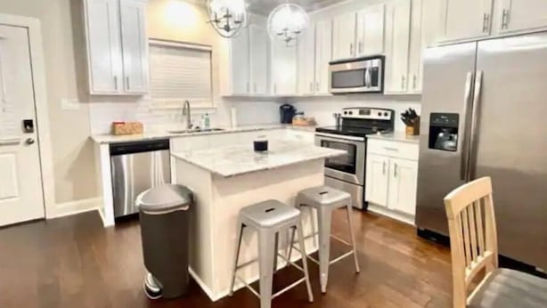 A modern kitchen with white cabinetry, stainless steel appliances, and a central island with stools. - Luxury Townhouse Near Lakefront & Downtown (Lake Charles)