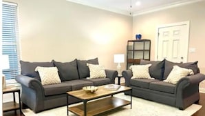 A living room with two grey sofas, a wooden coffee table, and a white rug. - Luxury Townhouse Near Lakefront & Downtown (Lake Charles)