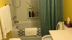 A bathroom with a bathtub, toilet, and sink. There are towels stacked on the floor and a shower curtain. - Gypsywind Home (Edmonton)