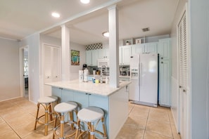 A kitchen with a central island, white cabinets, and a microwave. There are three wicker stools at the island.