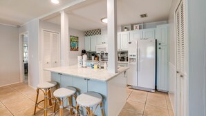 A kitchen with white cabinets, a marble countertop, and three wicker bar stools. - Golf Cart, Simpatico by SeaBreeze Vacation (Anna Maria)