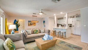A spacious living room with a sofa, a coffee table, and a kitchen area in the background. - Golf Cart, Simpatico by SeaBreeze Vacation (Anna Maria)