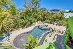 A swimming pool with a circular design, surrounded by a garden with various plants and a building in the background.