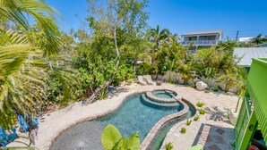 A swimming pool with a circular design, surrounded by tropical plants and a stone pathway. - Golf Cart, Simpatico by SeaBreeze Vacation (Anna Maria)