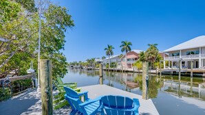 A waterfront property with a dock, blue Adirondack chairs, and a clear view of the water. - Golf Cart, Simpatico by SeaBreeze Vacation (Anna Maria)