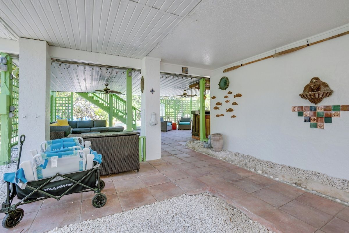 A covered patio area with a stroller, a wicker sofa, and a tiled wall with decorative fish.