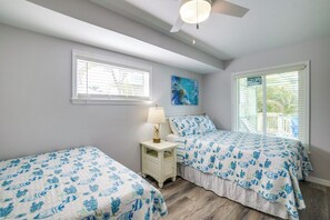 A bedroom with two beds, a nightstand, a ceiling fan, and a window with blinds.