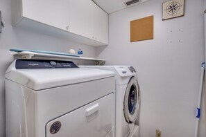 A laundry room with a front-loading washer and dryer, a shelf with a water bottle, and a compass on the wall.