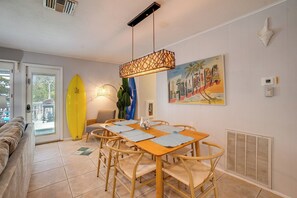 A dining area with a table and chairs, a surfboard, and a beach-themed painting.