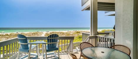 A covered outdoor area with a view of the beach, featuring a table and chairs, and a railing.