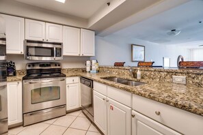 A kitchen with white cabinets, a stainless steel oven, a microwave, a granite countertop, and a sink.