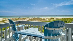 Une terrasse avec des chaises Adirondack bleues donnant sur une plage bordée de dunes de sable et sur l’océan.