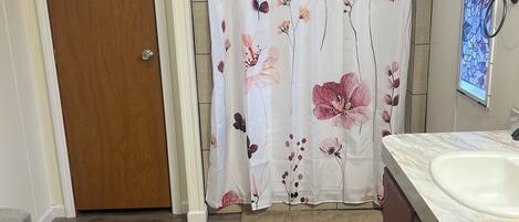 Un baño con puerta de madera, cortina de ducha con motivos florales, lavamanos y encimera de mármol.