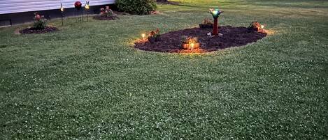 A well-maintained lawn with a small garden area featuring decorative lights and a central tree.