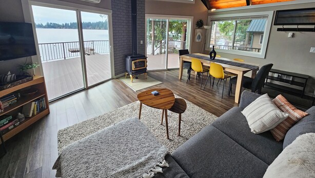 Een ruime woonkamer met een groot raam, een open haard, een eettafel met stoelen en een bank.