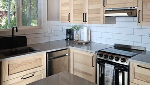 Een moderne keuken met houten kasten, een roestvrijstalen fornuis en een raam met uitzicht op bomen.