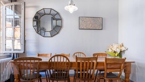 Un comedor con mesa y sillas de madera, un espejo hexagonal y una obra enmarcada en la pared.
