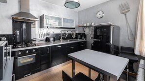 Una cocina moderna con armarios negros, una estufa de acero inoxidable, una máquina de café y un comedor con mesa y sillas.