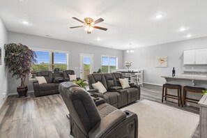 A spacious living room with a large sectional sofa, a ceiling fan, and a view of the outdoors. - Gated Golf Community, Private Hot Tub, Arcade, Updated Kitchen & Free Tickets Near SDC (Branson West)