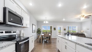 A modern kitchen with white cabinets, a built-in microwave, a stove, and a dining area with a table and chairs. - Bright Open Floorplan with Hot Tub, Private Deck, Arcade, Golf Course & High-End Decor (Branson West)