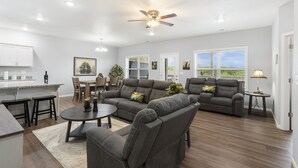 A spacious living room with a sectional sofa, a dining area, and a kitchen. - Bright Open Floorplan with Hot Tub, Private Deck, Arcade, Golf Course & High-End Decor (Branson West)