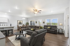 A spacious living room with a sectional sofa, a dining area, and a kitchen. - Bright Open Floorplan with Hot Tub, Private Deck, Arcade, Golf Course & High-End Decor (Branson West)