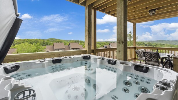 A hot tub on a wooden deck with a view of green hills and houses. - Bright Open Floorplan with Hot Tub, Private Deck, Arcade, Golf Course & High-End Decor (Branson West)