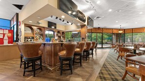 A bar area with a counter, stools, and a view through large windows. - Stonebridge Resort Condo w Onsite Golf_Private Hot Tub_Outdoor Pool_Free Tickets (Branson West)