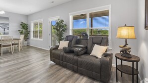 A living room with a dark brown leather sofa, a dining table with chairs, and a lamp on a side table. - Stonebridge Resort Condo w Onsite Golf_Private Hot Tub_Outdoor Pool_Free Tickets (Branson West)