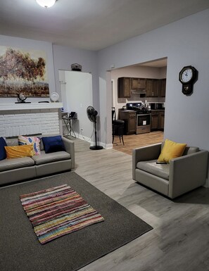Cozy living space with a beige sofa, armchair, and colorful rug, featuring a large abstract painting above the fireplace.