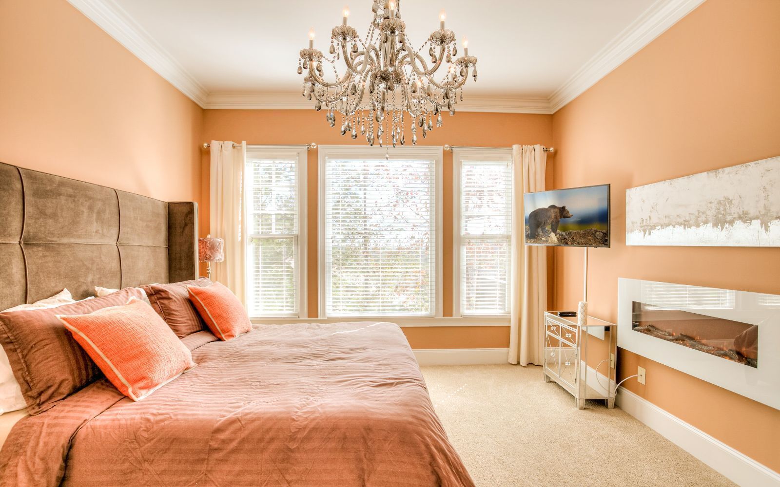 A bedroom with a large bed, a chandelier, a fireplace, and a TV on the wall.