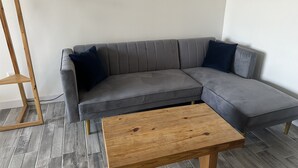 Een grijze modulaire bank met twee donkerblauwe kussens, een houten salontafel en een vloerlamp van hout.