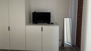 Een kamer met een witte garderobe, een flatscreen televisie op een klein kastje, en een spiegel die een bakstenen muur weerkaatst.