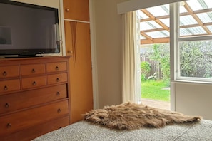 Ein Zimmer mit einem Holzschrank, einem Fernseher darauf, einem Fellteppich auf dem Boden und einem Fenster mit Blick auf einen Garten.