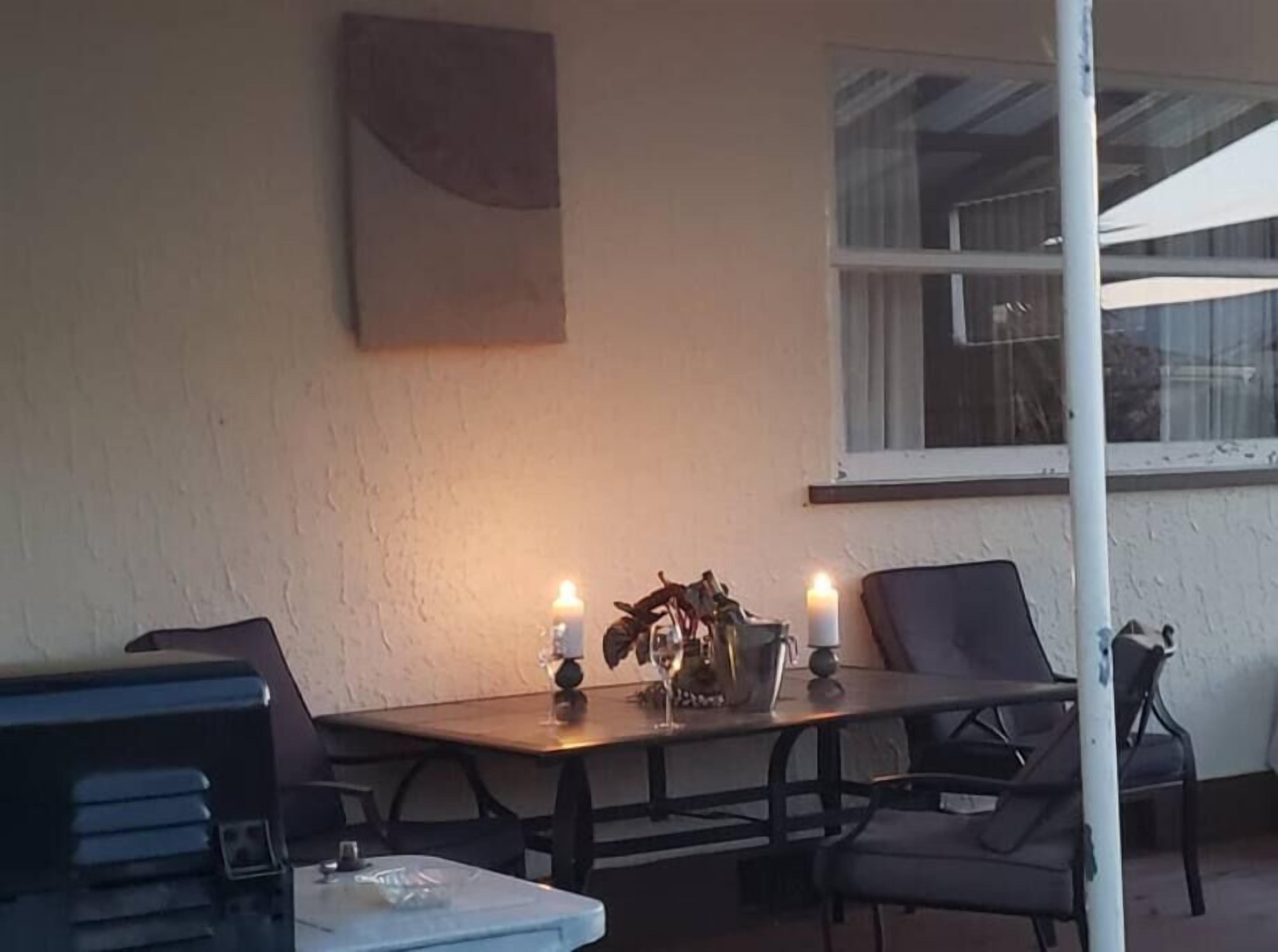 En udendørs spiseplads med et bord, stole, stearinlys og en potteplante.