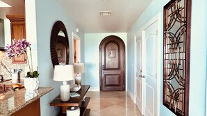 Un corridoio con pavimento in marmo, una porta in legno, uno specchio decorativo e un punto luce a parete.