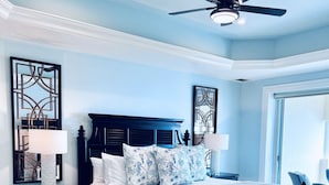 Una camera da letto con un letto in legno scuro, biancheria bianca, una ventola a soffitto e un'ampia finestra.