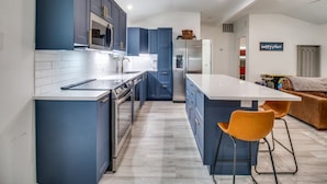 Een moderne keuken met blauwe kastjes, een wit aanrechtblad en een centraal eiland met twee oranje stoelen.