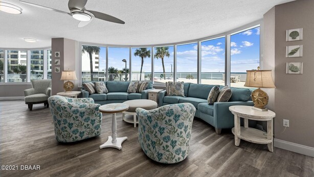 A spacious living room with a curved ceiling, large windows offering a view of the beach, and a ceiling fan.